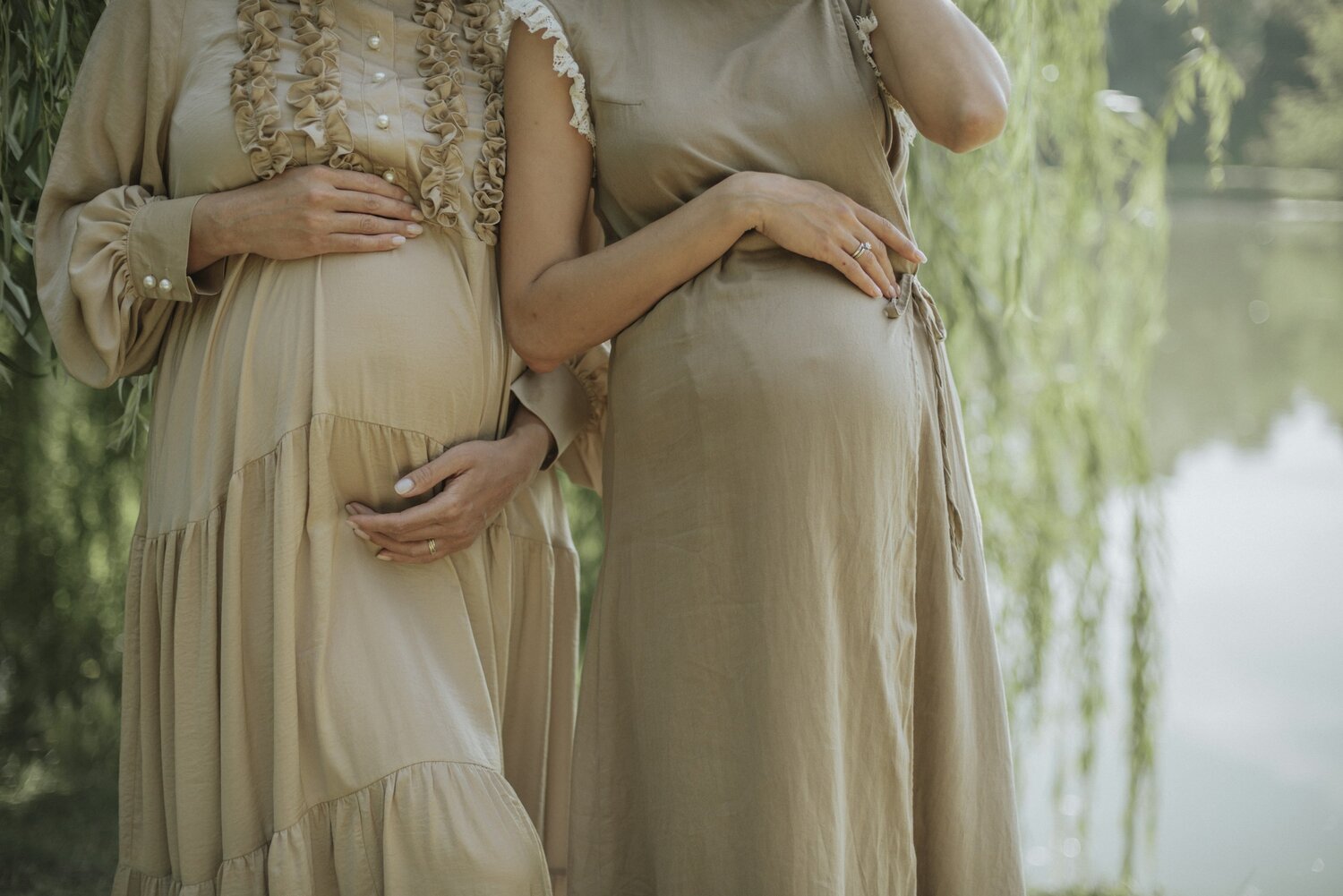 Two pregnant women standing together outdoors, hands resting on their bellies