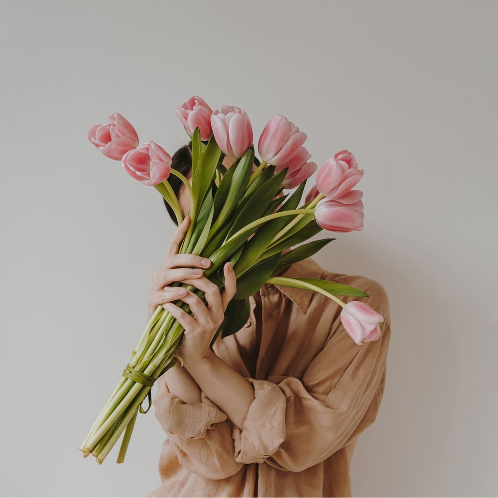 A woman holding a bunch of pink tulips in front of her face